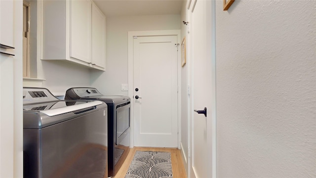 clothes washing area with cabinets, light wood-type flooring, and washer and clothes dryer