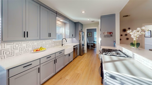 kitchen featuring gray cabinetry, sink, stainless steel appliances, light hardwood / wood-style flooring, and decorative backsplash