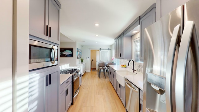 kitchen with a barn door, sink, gray cabinetry, and stainless steel appliances