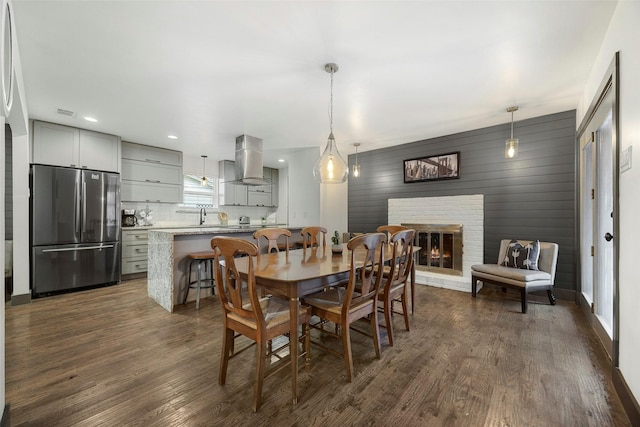 dining room with dark hardwood / wood-style floors, sink, wooden walls, and a brick fireplace