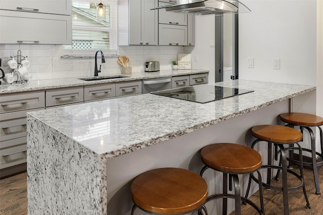 kitchen with a kitchen bar, sink, light stone countertops, dark hardwood / wood-style flooring, and extractor fan