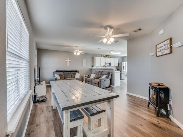 dining area with ceiling fan, a wood stove, and light hardwood / wood-style flooring