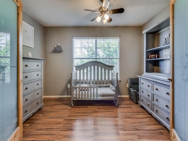 bedroom featuring dark hardwood / wood-style flooring, a nursery area, and ceiling fan