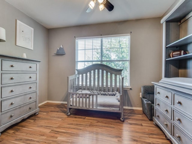 bedroom with ceiling fan, a nursery area, and wood-type flooring