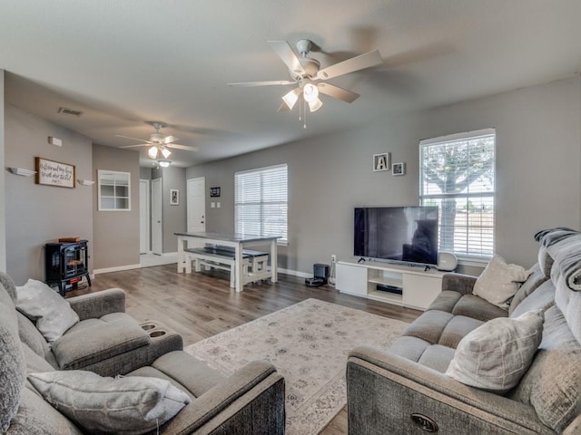 living room featuring ceiling fan, wood-type flooring, and a wood stove