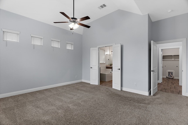 unfurnished bedroom featuring ceiling fan, connected bathroom, high vaulted ceiling, and dark colored carpet