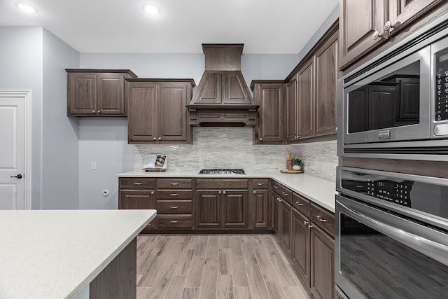 kitchen featuring backsplash, dark brown cabinets, premium range hood, and appliances with stainless steel finishes