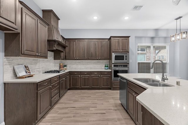 kitchen featuring decorative light fixtures, sink, custom exhaust hood, dark brown cabinetry, and stainless steel appliances