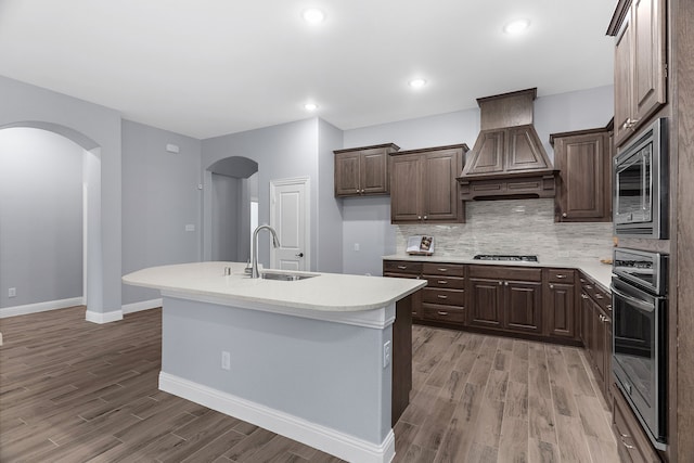 kitchen featuring sink, custom exhaust hood, hardwood / wood-style flooring, stainless steel appliances, and a center island with sink