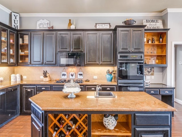 kitchen with light stone countertops, multiple ovens, dark brown cabinets, a kitchen island with sink, and sink