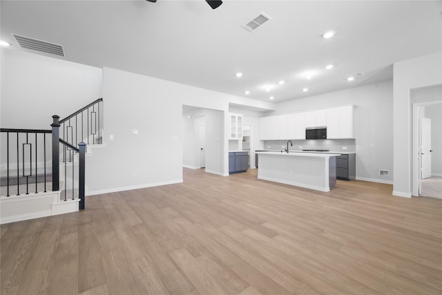 kitchen with sink, light hardwood / wood-style flooring, a kitchen island with sink, white cabinets, and decorative backsplash