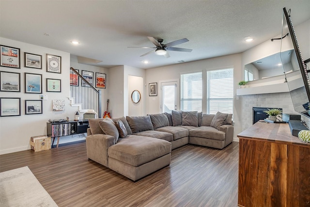 living room featuring a textured ceiling, dark hardwood / wood-style flooring, a brick fireplace, and ceiling fan