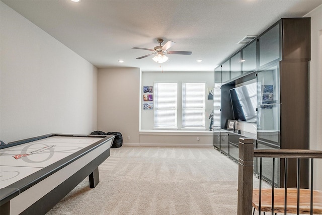 game room featuring light carpet, ceiling fan, and a textured ceiling