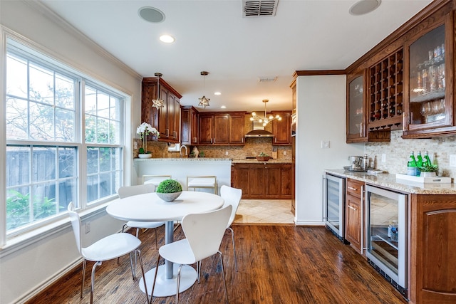 dining space with ornamental molding, an inviting chandelier, wine cooler, and dark wood-type flooring