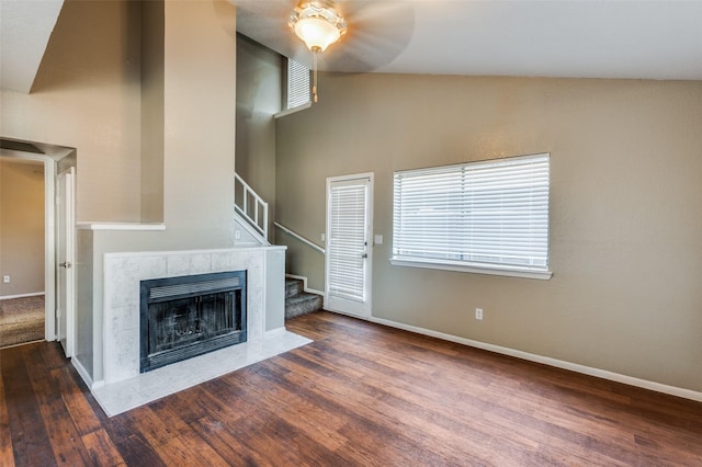 unfurnished living room with a tiled fireplace, ceiling fan, a healthy amount of sunlight, and dark hardwood / wood-style floors