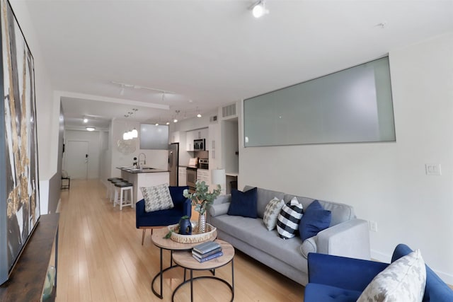 living room featuring sink, rail lighting, and light wood-type flooring