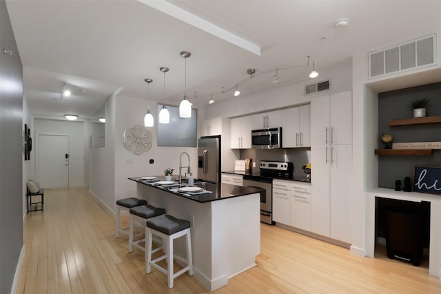 kitchen featuring white cabinets, pendant lighting, light wood-type flooring, and stainless steel appliances