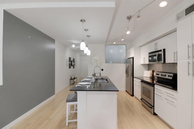 kitchen with a kitchen island with sink, sink, hanging light fixtures, white cabinetry, and stainless steel appliances