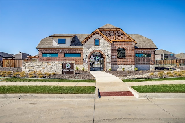 view of front of property featuring stone siding, brick siding, a shingled roof, and fence