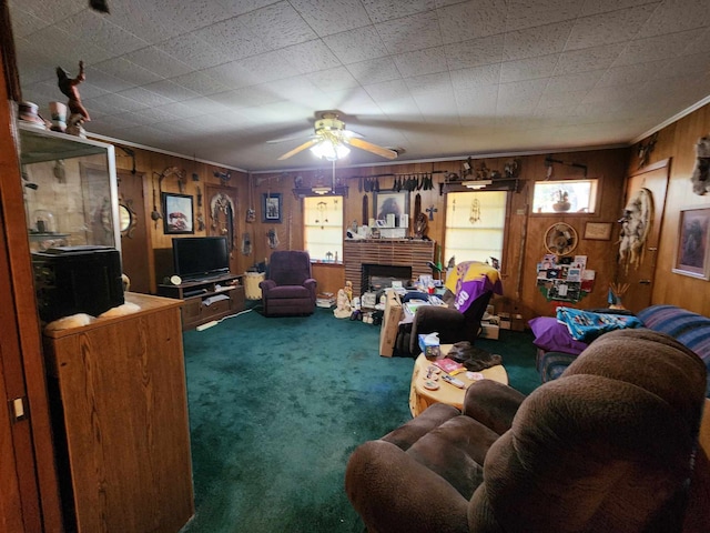 living room featuring carpet, wooden walls, ceiling fan, a fireplace, and plenty of natural light