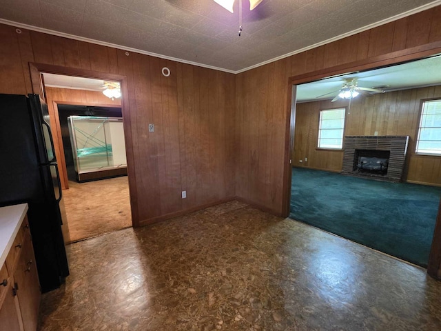 unfurnished living room featuring wooden walls, ornamental molding, ceiling fan, and carpet