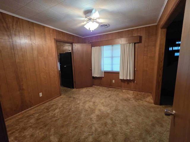 unfurnished bedroom featuring crown molding, freestanding refrigerator, carpet, and wooden walls