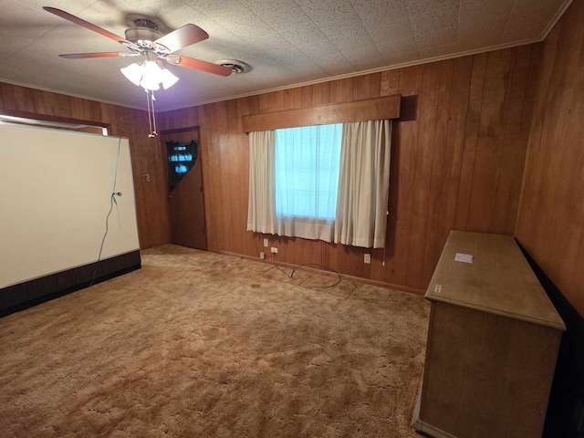 unfurnished bedroom featuring wooden walls, carpet floors, ceiling fan, and ornamental molding
