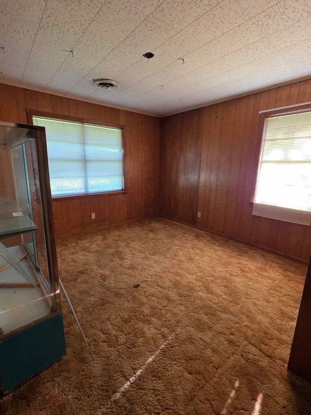 carpeted spare room featuring visible vents and wood walls