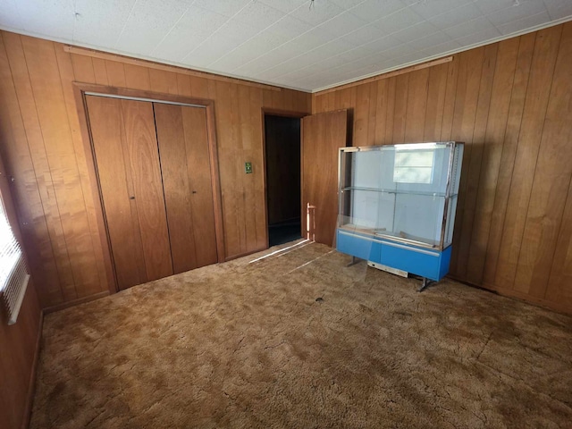 unfurnished bedroom featuring a closet, wooden walls, and carpet floors