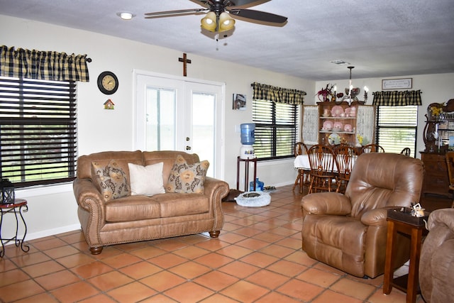 tiled living room with a textured ceiling, french doors, a healthy amount of sunlight, and ceiling fan with notable chandelier