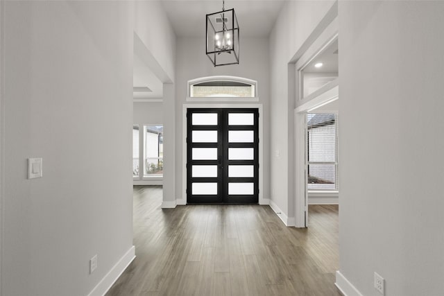 foyer with french doors, an inviting chandelier, a towering ceiling, and wood-type flooring