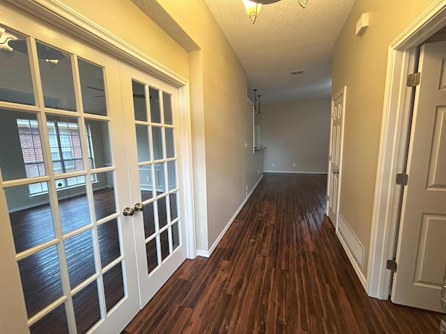 corridor with french doors, a textured ceiling, and dark hardwood / wood-style flooring