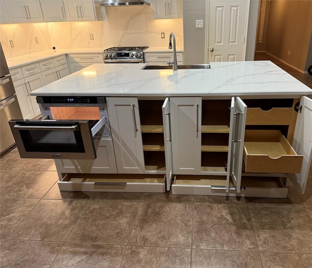 kitchen featuring light stone counters, a kitchen island with sink, stainless steel range oven, and sink