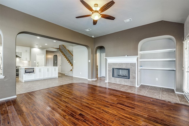 unfurnished living room with lofted ceiling, sink, ceiling fan, a tiled fireplace, and hardwood / wood-style floors