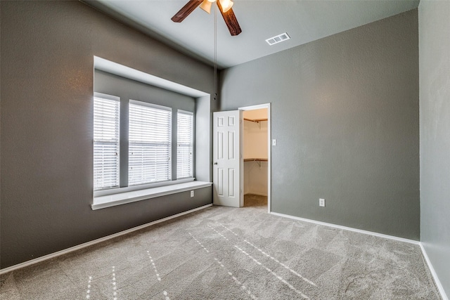 unfurnished bedroom with light carpet, a walk in closet, a closet, and ceiling fan