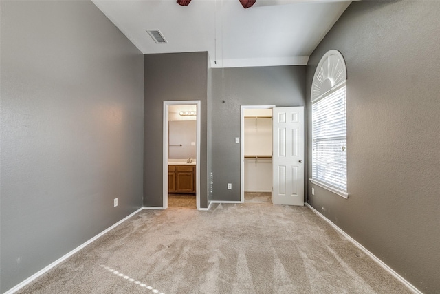 unfurnished bedroom featuring ensuite bath, a spacious closet, light colored carpet, a closet, and ceiling fan