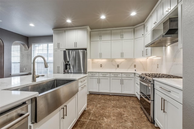 kitchen featuring white cabinetry, decorative backsplash, stainless steel appliances, and wall chimney exhaust hood