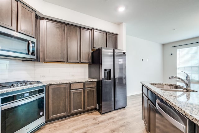 kitchen featuring light stone countertops, sink, stainless steel appliances, light hardwood / wood-style floors, and decorative backsplash