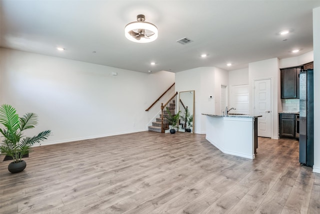 kitchen with stainless steel refrigerator, light stone counters, sink, and light wood-type flooring