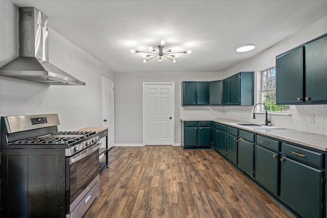 kitchen featuring sink, stainless steel gas stove, dark wood-type flooring, wall chimney range hood, and an inviting chandelier