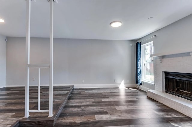 unfurnished living room featuring dark wood-type flooring and a brick fireplace