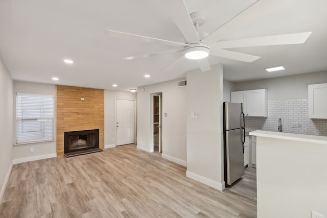 unfurnished living room featuring ceiling fan, a large fireplace, light hardwood / wood-style floors, and sink