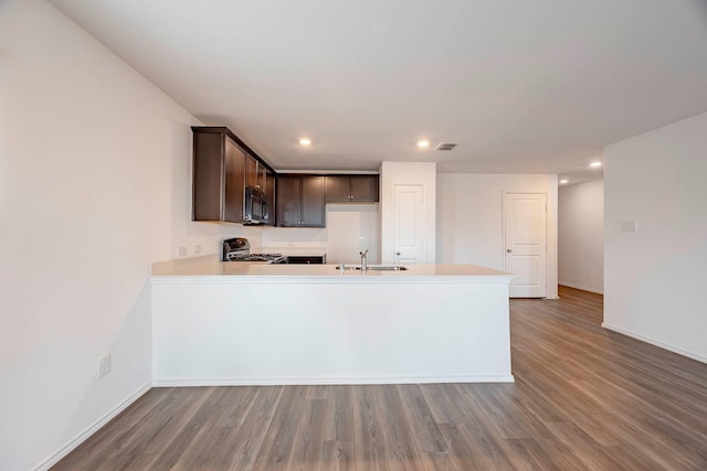 kitchen featuring sink, kitchen peninsula, stove, dark brown cabinets, and hardwood / wood-style flooring