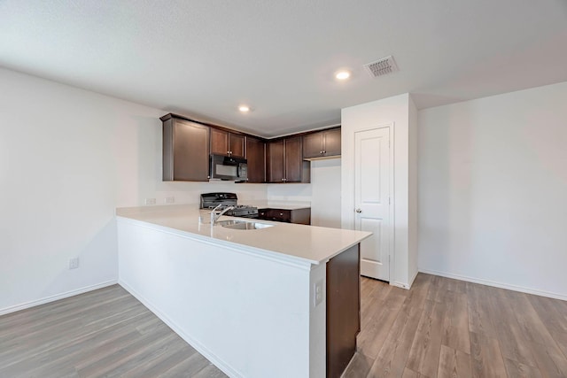 kitchen with kitchen peninsula, light hardwood / wood-style floors, dark brown cabinetry, and sink