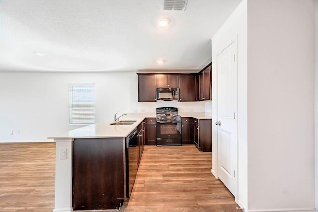 kitchen with black appliances, kitchen peninsula, sink, light hardwood / wood-style flooring, and dark brown cabinetry