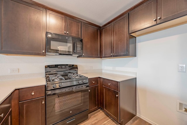 kitchen with black appliances, dark brown cabinets, and light hardwood / wood-style flooring