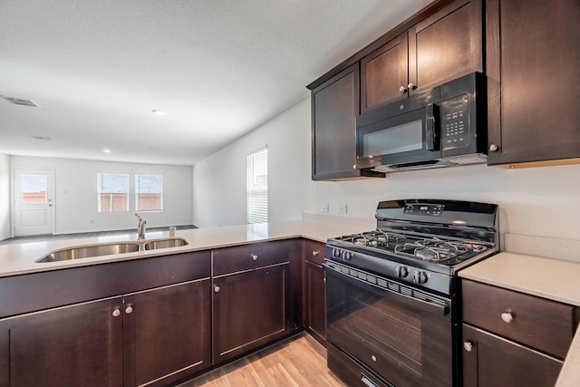 kitchen with kitchen peninsula, light wood-type flooring, dark brown cabinetry, sink, and black appliances