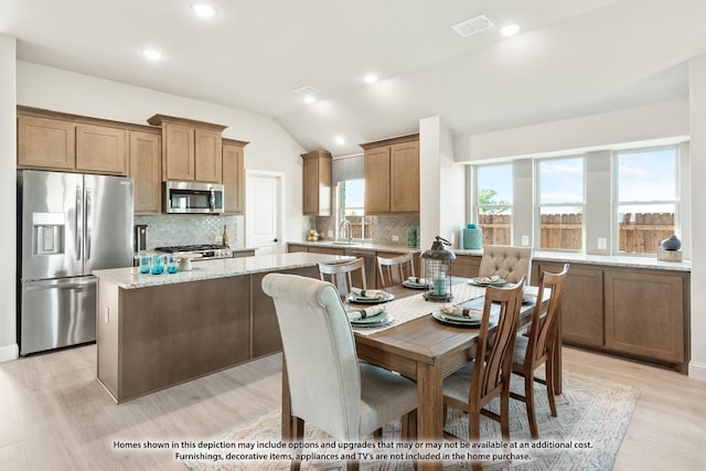 kitchen with sink, light stone counters, lofted ceiling, a kitchen island, and appliances with stainless steel finishes