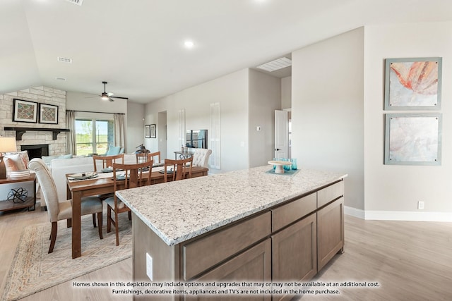 kitchen featuring light stone countertops, ceiling fan, a center island, light hardwood / wood-style floors, and a stone fireplace