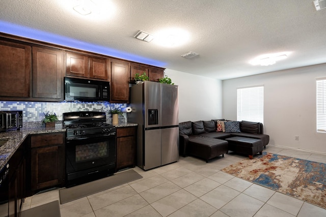 kitchen featuring dark brown cabinetry, dark stone counters, light tile patterned floors, and black appliances